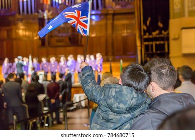 Dad Holding His Child Waving An Australian Flag During An Australian Citizenship Ceremony.