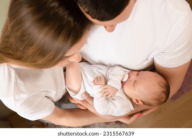 papá sostiene a un bebé con un pacificador en sus brazos, retrato de un bebé. padres jóvenes sostienen al bebé en sus brazos. papá y mamá abrazan a un niño pequeño. la familia feliz relajándose en casa.