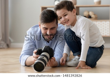 Dad holds photo camera explains teaches his little son how take photo create make art spend time together on warm floor, amateur or professional photographer share knowledge education of child concept