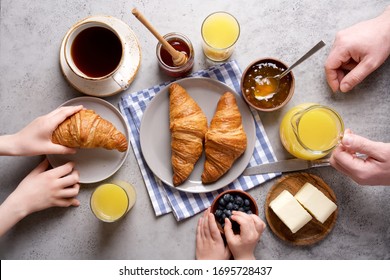 Dad With Kids Eating Breakfast In The Morning. Top View Of A Gray Table, Croissants, Orange Juice, Coffee, Jam And Butter. Stay Home Concept