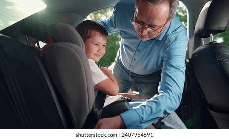 Dad lifts his boy out of the safety car seat. Happy family. Father secures her kid son in car seat using child safety belt. Family road trip Dad cares about her son safety Child sits in car child seat