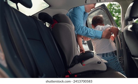 Dad lifts his boy out of the safety car seat. Happy family. Father secures her kid son in car seat using child safety belt. Family road trip Dad cares about her son safety Child sits in car child seat
