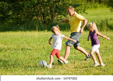 Dad And Little Daughters Playing Soccer On A Green Meadow