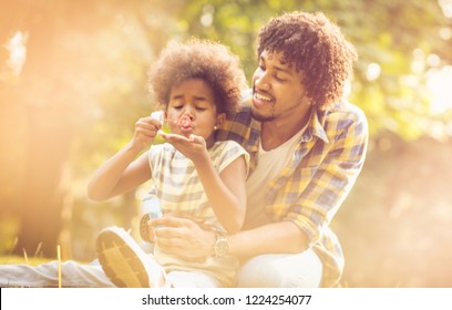 Dad Look, This Is Fun. African American Daughter And Her Father Playing With Water Balloons In Park.