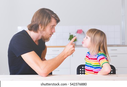 Dad Looking Angry Arguing With His Daughter In Preschool Age Sitting On Kitchen At Home