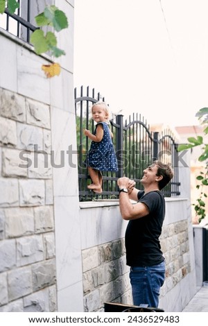 Dad looks at a little girl standing on a metal fence