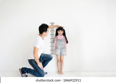 Dad measures growth of her child daughter at blank white brick wall