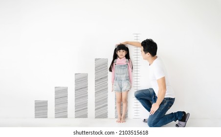 Dad measures height increase of her child daughter at white brick wall with graph growing growth