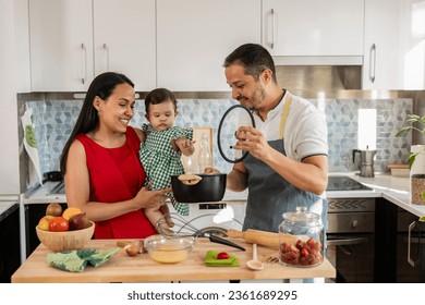 dad and mom cooking at home with baby in arms - beautiful Latin American family preparing delicious food in the kitchen - - Powered by Shutterstock