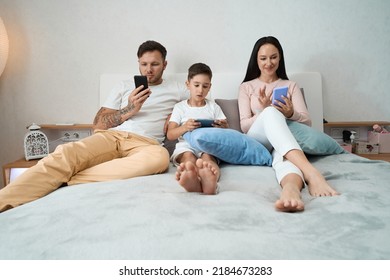 Dad, Mom And Son Sat On The Bed With Smartphones