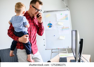 Dad Must To Work From Home And Cares Of Little Kid. Busy Father Is Answering The Phone Calls With A Toddler Son On His Arms