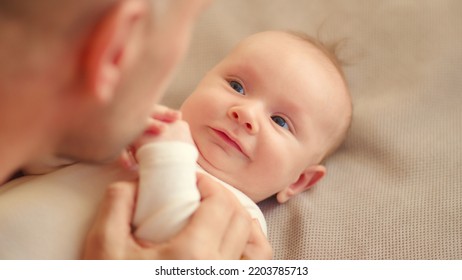 Dad Playing With A Newborn Baby. Cute Baby Is Trying To Pronounce Sounds While Looking At His Dad. Face Of An Active Caucasian Baby Looking At A Parent. Father Is Playing With His Baby.