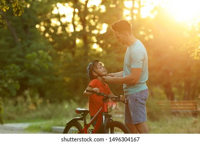 Dad Putting Bicycle Helmet On Son In Park On Sunny Day