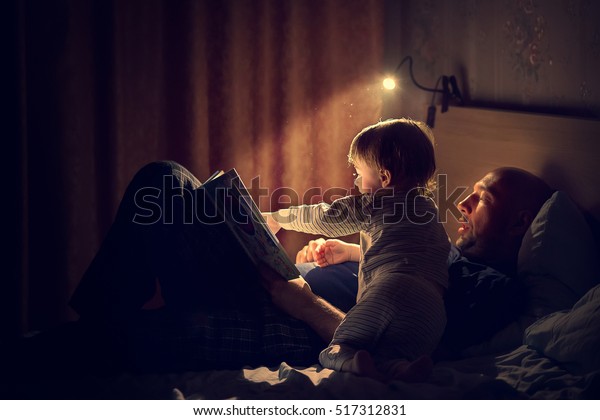 Dad is\
reading a bedtime story to his little son. Night lamp is shine\
beautifully. Image with selective focus and\
toning