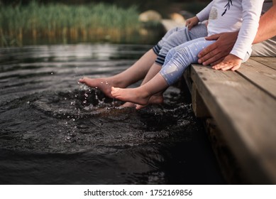 Dad is sitting with a child on a pier on the lake and splashing water. Bare feet in the water.