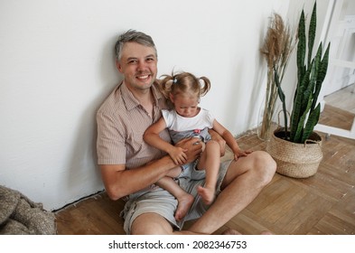 Dad Is Sitting On The Floor And Holding A Little Crying Girl In His Arms. Caring Father