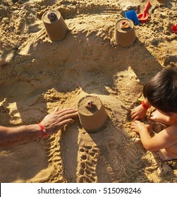 Dad And Son Build Towers Out Of The Sand On The Beach Summer Vacation On The Sea In The Resort View From Above. Men And Children Hands.