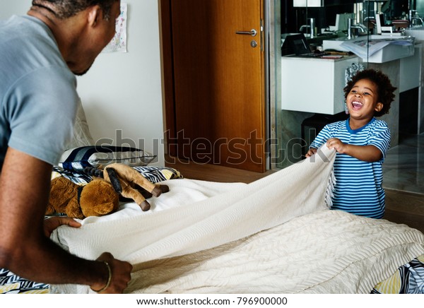 Dad and son changing\
bed sheet together