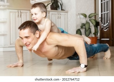 Dad And Son Do Push-ups From The Floor In The Room Of The House. The Child Lies On His Father's Back. Physical Activity At Home. A Good Role Model. A Man And A Boy Play Sports At Home.