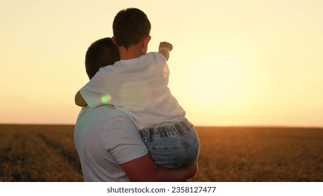 Dad, son in field watching sunset. Father and child stretch their hand to sun, kid plays with dad. Concept of happy family, unity with nature. Walk son, dad outdoor. Child is in arms of father, family - Powered by Shutterstock