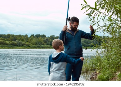 Dad And Son Are Fishing. Sunset. We Caught A Fish. The Boy Reaches Out To Grab The Fish. 