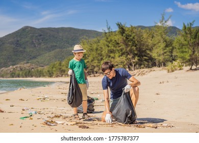 Dad And Son In Gloves Cleaning Up The Beach Pick Up Plastic Bags That Pollute Sea. Natural Education Of Children. Problem Of Spilled Rubbish Trash Garbage On The Beach Sand Caused By Man-made