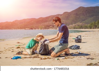 Dad And Son In Gloves Cleaning Up The Beach Pick Up Plastic Bags That Pollute Sea. Natural Education Of Children. Problem Of Spilled Rubbish Trash Garbage On The Beach Sand Caused By Man-made