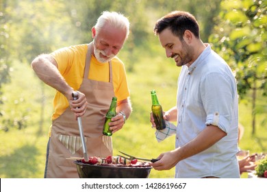 Dad And Son Make Barbecue And Drink Beer In Garden.