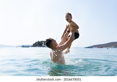 父と息子は海で遊んでいる。父は息子を育て上げる。ギリシャの島々、水しぶき、休暇、青い空、晴れた日