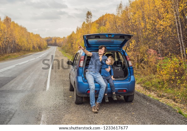 Dad and son are resting on the\
side of the road on a road trip. Road trip with children\
concept