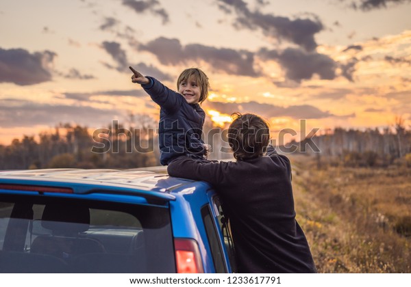 Dad and son are resting on the\
side of the road on a road trip. Road trip with children\
concept