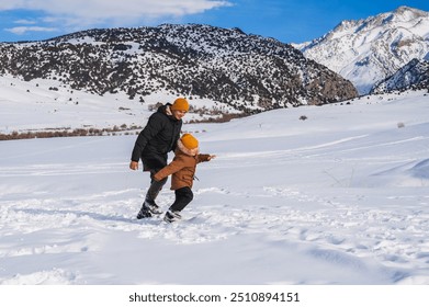 Dad and son run along a snow-covered slope against the backdrop of a mountain landscape in winter. - Powered by Shutterstock