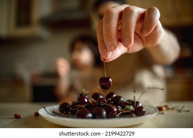 Dad And Son Sit In The Kitchen At Home And Eat Cherries. The Concept Of A Happy Family. Shallow Depth Of Field