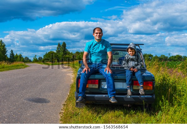 dad and son sitting on the back of a car\
near the road. dad and son travel by\
car