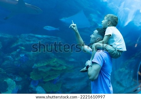 Dad and son spend time together in the Aquarium. Son sits on dad's back and explores the underwater world