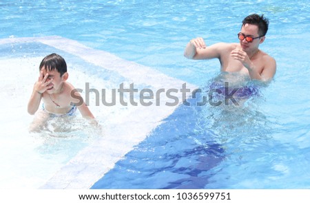 Dad and son are swimming together in the summer.
