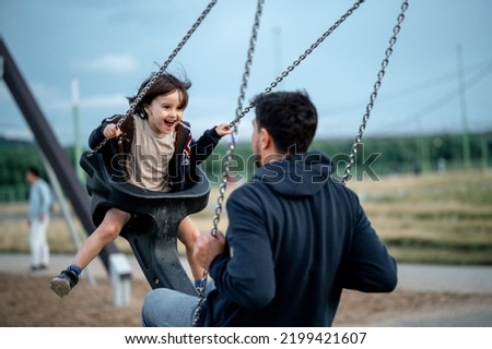 Dad and son swing on a swing. Happy family. The father spends time with the children, the father walks with the child in the summer in the park