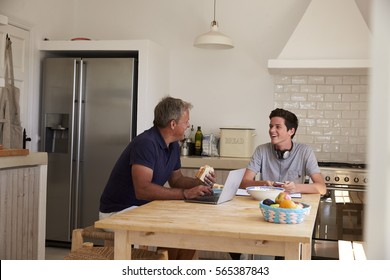 Dad And Son Using Technology Eat And Talk At Kitchen Table