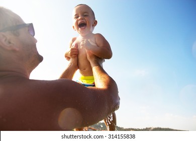 Dad Standing In The Sea And Holding A Smiling Baby Boy In Air