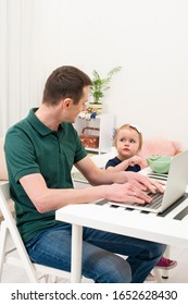 Dad Take Care Of A Little Daughter At Home.  He Gave Her Cereal With Milk And Started Working Using A Laptop. Life Style.  The Modern Role Of Men In The Family.