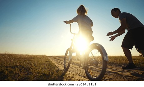 dad teaches daughter to ride a bike. happy family childhood dream concept. father and little daughter learn to ride bike silhouette in the park. happy family goes in for sunlight sports outdoors - Shutterstock ID 2361451151