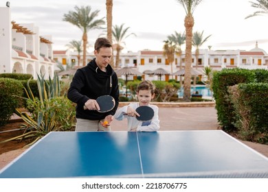 Dad teaches son to play table tennis on vacation at the hotel. The coach and the child are playing ping pong. Sports life active lifestyle. Parenthood fatherhood together. Active outdoor activities. - Powered by Shutterstock