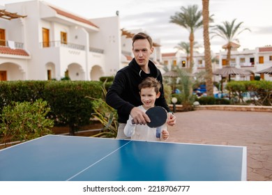 Dad teaches son to play table tennis on vacation at the hotel. The coach and the child are playing ping pong. Sports life active lifestyle. Parenthood fatherhood together. Active outdoor activities. - Powered by Shutterstock