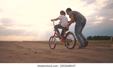 dad teaches son to ride a bike. happy family kid dream concept. the boy sat on bicycle for the first time, his father teaches boy to ride a bicycle. lifestyle dog runs with family, fun family pastime - Powered by Shutterstock