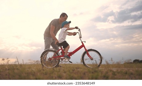 dad teaches son to ride a bike. happy family kid dream concept. the boy sat on bicycle for the first time, his father teaches boy to ride a bicycle. dog runs with lifestyle family, fun family pastime - Powered by Shutterstock