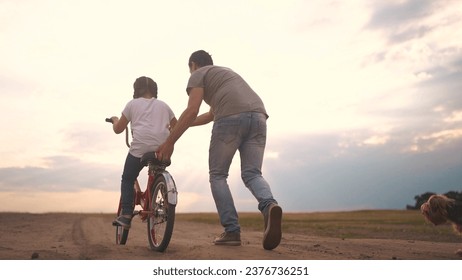 dad teaches son to ride a bike. happy family kid dream concept. the boy sat on bicycle for the first time, his father teaches boy to ride a bicycle. dog lifestyle runs with family, fun family pastime - Powered by Shutterstock