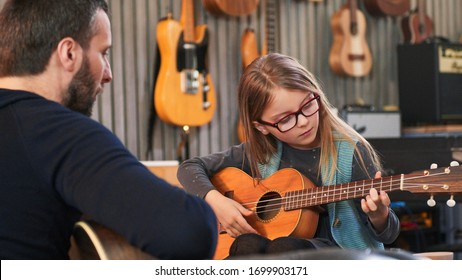 Dad teaching guitar and ukulele to his daughter.Little girl learning guitar at home.Close up.Ukulele class at home. Child learning guitar from her father - Shutterstock ID 1699903171