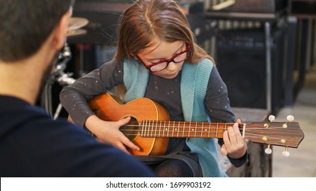 Dad teaching guitar and ukulele to his daughter.Little girl learning guitar at home.Close up.Ukulele class at home. Child learning guitar from her father - Powered by Shutterstock