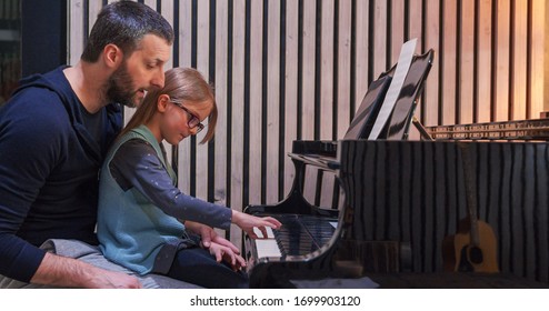 Dad teaching piano to his daughter.Little girl learning piano at home.Side view.Piano class at home. Child learning piano from her father