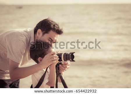 Dad is teaching son taking a photo at the beach at sunset with vintage color tone

